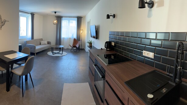 Een moderne keuken met een ingebouwde kookplaat, een eethoek met tafel en stoelen, een bank en een groot raam.