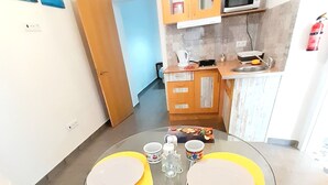 Un coin repas avec une table en verre, des chaises jaunes et vertes, et une cuisine en arrière-plan.