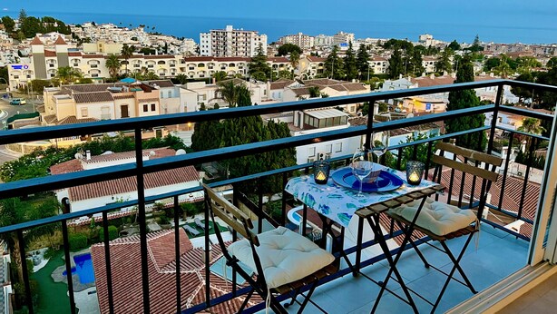 Un balcón con una mesa para dos, con vistas a una ciudad costera con edificios y cielo despejado.