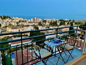 Un balcón con una mesa para dos, con vistas a una ciudad costera con edificios y cielo despejado.