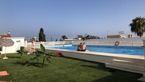 Una piscina bajo un cielo azul despejado, un flotador y una palmera.