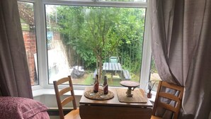A room with a wooden table and two chairs, a window with a view of a garden, and a bed with a pink blanket. - Private Studio Flat Great Location in Manchester (Manchester)