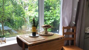 A wooden table with a bottle of wine, two glasses, and a plate of cookies by a window with a view of greenery. - Private Studio Flat Great Location in Manchester (Manchester)
