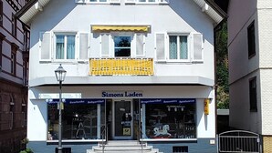 A two-story building with a white facade and yellow awning. The ground floor has a shop with a sign reading "Simons Laden."