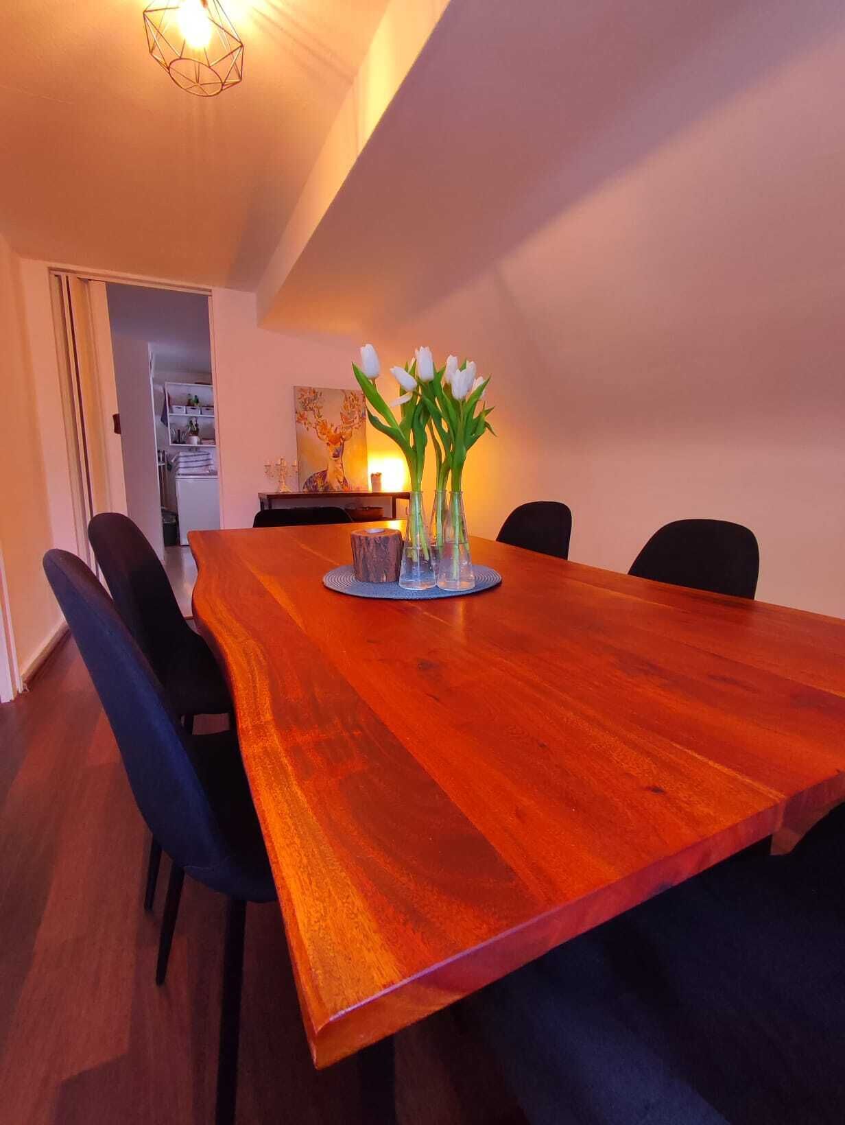 A dining area with a wooden table, four chairs, and a vase with white flowers.