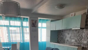Una sala moderna con un sofá seccional gris, una mesa de comedor con sillas y una cocina con armarios verde azulado.