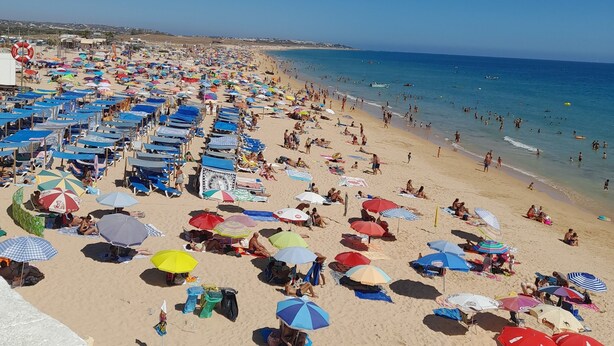 Una playa concurrida, con muchos sombrillas de colores y gente relajándose sobre la arena.