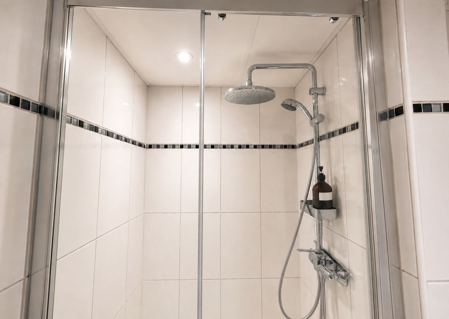 Una ducha con cerramiento de vidrio, cabezal de ducha manual y llave empotrada en la pared.