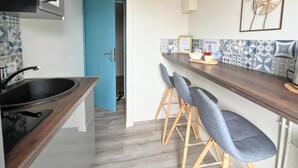 A modern kitchen with a blue door, a sink, and bar stools. - Apart'Moment SMART - Le Nid Douillet (Bourbourg)
