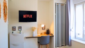 A modern room with a desk, chair, and a TV displaying 'NETFLIX'. - Apart'Moment SMART - Le Nid Douillet (Bourbourg)