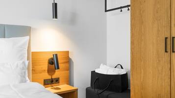 A neatly arranged hotel room with a bed, bedside table, lamp, and a wooden wardrobe.