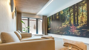 A modern living room with a sofa, a round wooden table with a candle, and a large forest-themed wall mural. - zeitlang by Rösslwirt (Lam)