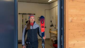 A person holding skis in a room with a wooden door, a wall-mounted rack, and a table with items on it.