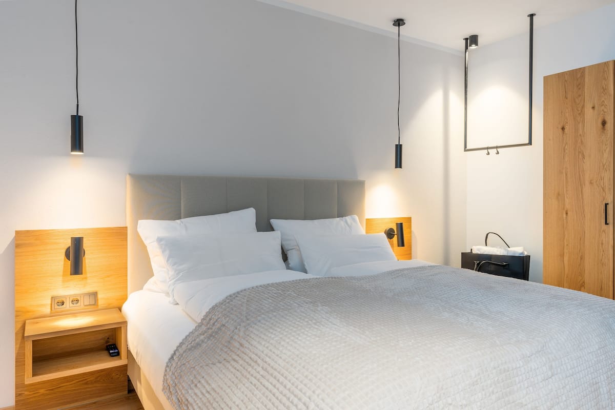 Ein modernes Schlafzimmer mit Bett, Nachttischen, einem Kleiderschrank und Pendelleuchten.
