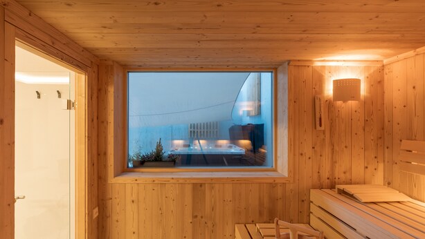 A wooden sauna room with a bench, a window, and a wall-mounted light fixture. - zeitlang by Rösslwirt (Lam)
