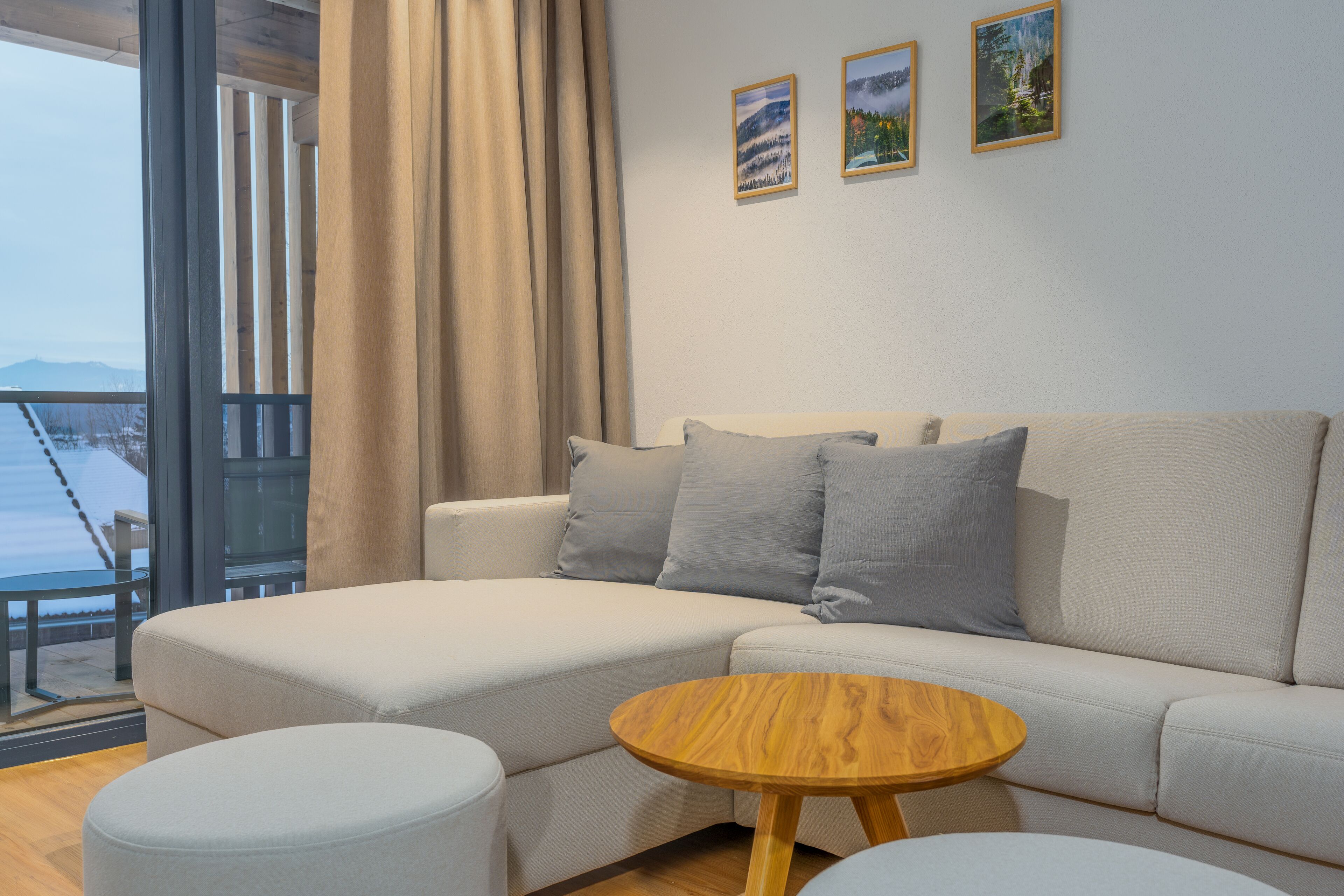 A modern living room with a sofa, ottoman, and a small wooden table. There are three framed pictures on the wall.