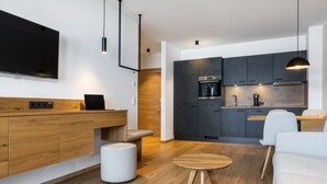 A modern kitchen with dark cabinets, a built-in oven, and a coffee machine. There is a wooden bench and a round wooden table in the living area. - zeitlang by Rösslwirt (Lam)