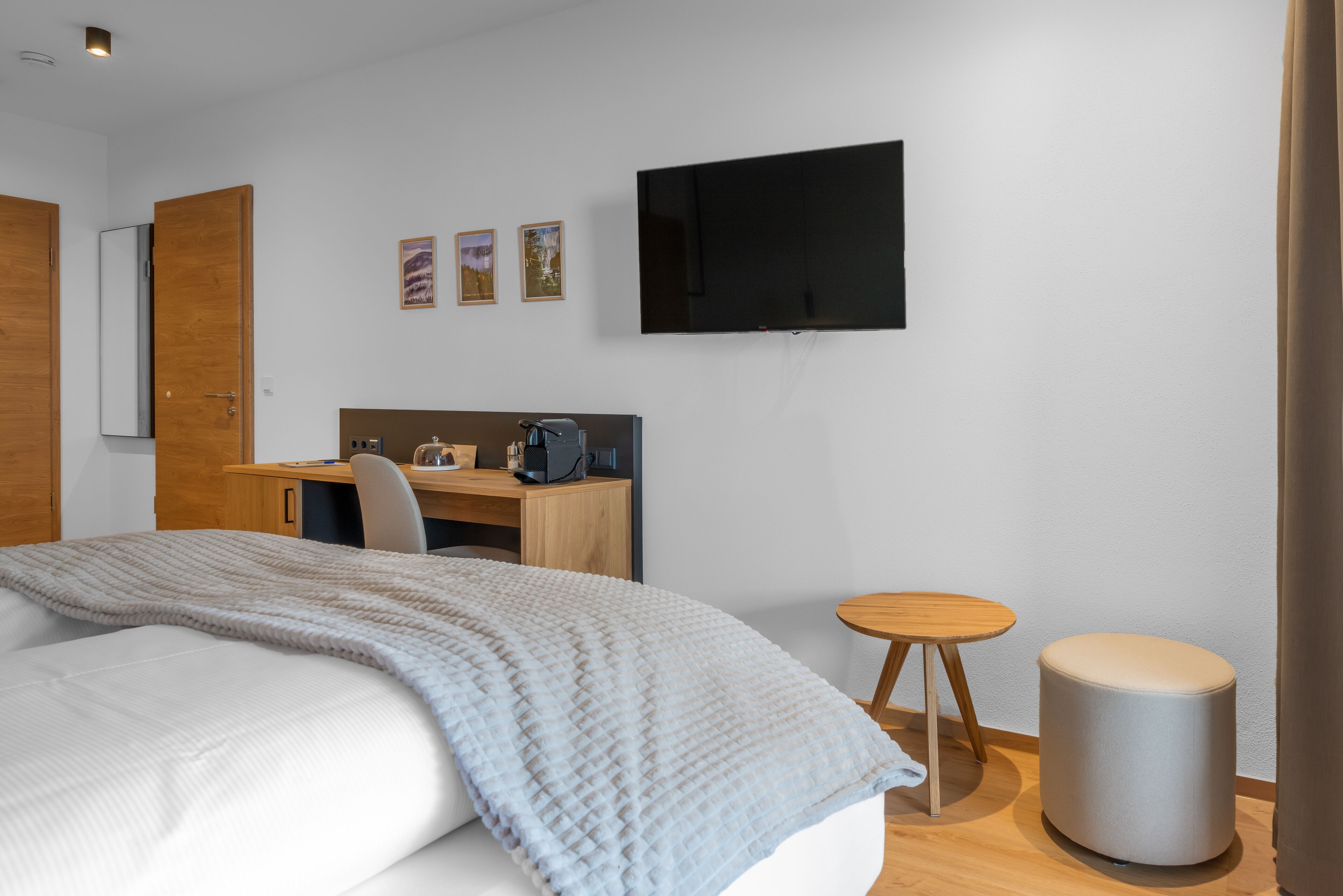 Una habitación de hotel moderna con cama, escritorio, silla, televisor y un taburete pequeño.