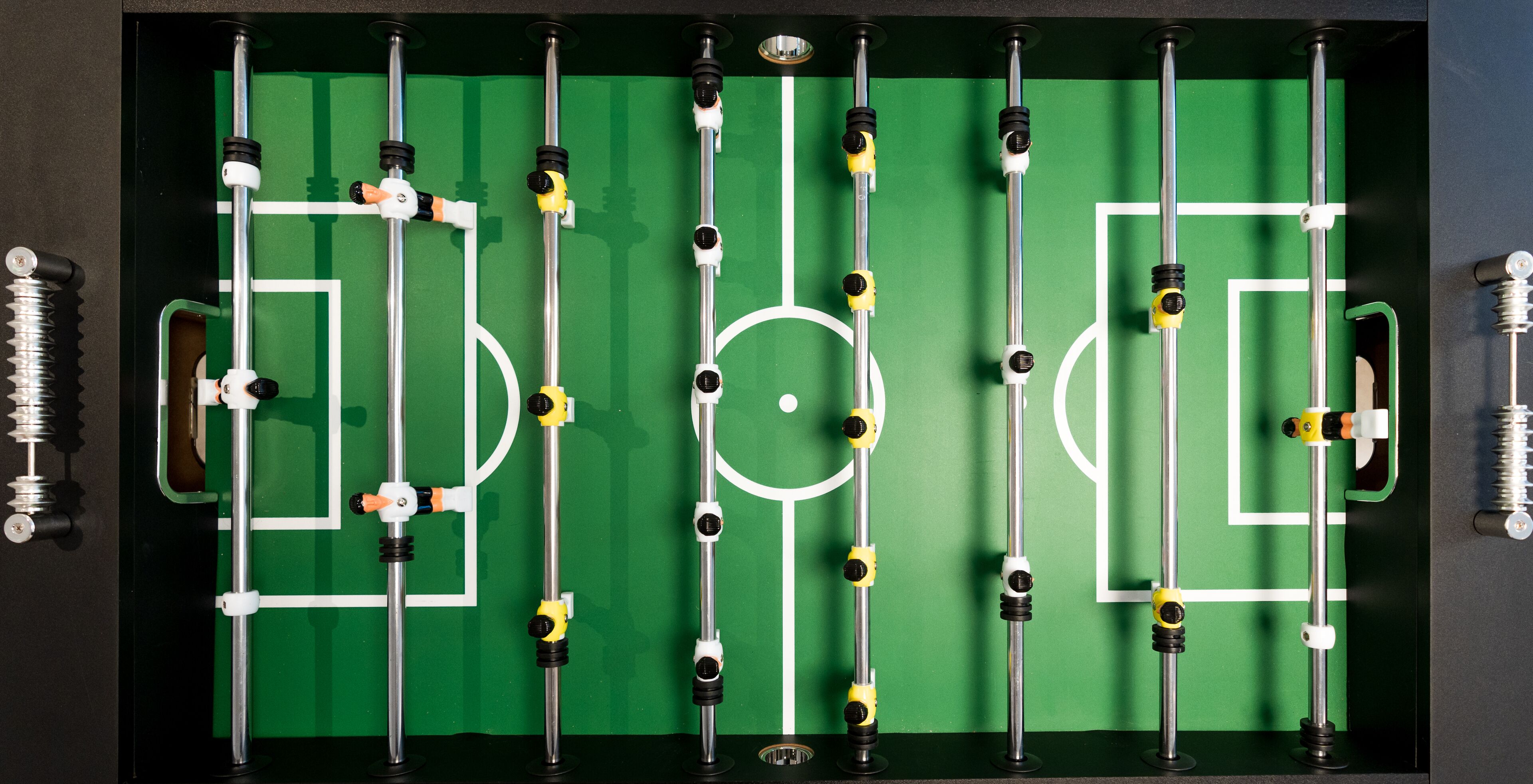 A tabletop foosball table with a green playing surface and white boundary lines.