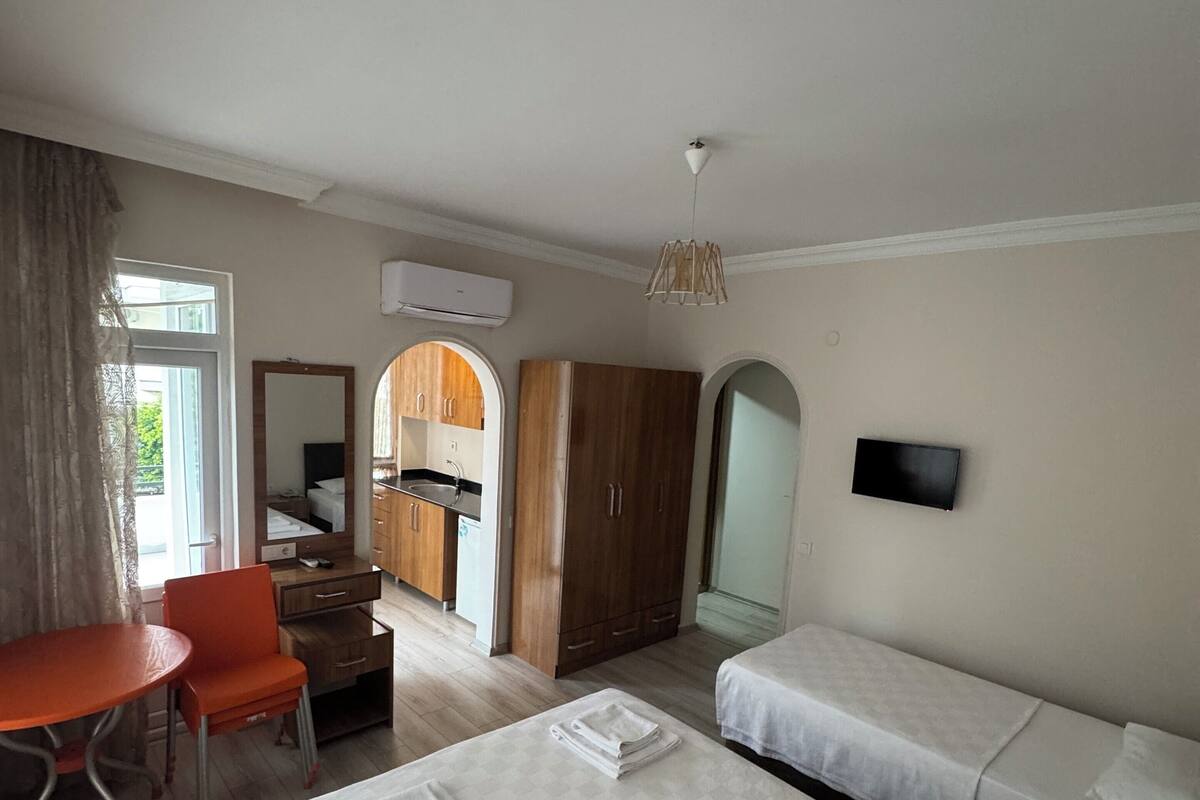A hotel room with two beds, a desk, a chair, a TV, and a kitchenette.