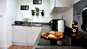 A modern kitchen with white cabinetry, a black countertop, and a glass-top stove. There are potted plants on the wall, a sink, and a variety of food items on the counter. - Remarkable 2-bed Apartment in Leafy Sefton Park (Liverpool)