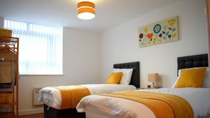 A hotel room with two beds, a bunk bed, a window with blinds, a radiator, and a wall art piece. - Remarkable 2-bed Apartment in Leafy Sefton Park (Liverpool)