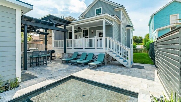 Una casa con porche cubierto, mobiliario exterior y piscina.