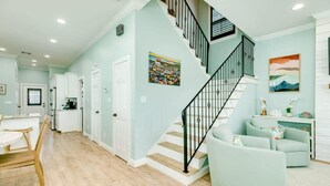 Un amplio salón con escalera, paredes azul claro y una cocina al fondo.