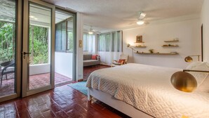 Une chambre dotée d’un grand lit, d’une porte-fenêtre coulissante donnant sur un balcon, d’un ventilateur de plafond et d’une table de chevet avec une lampe.