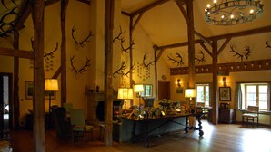 A spacious room with wooden beams, a large chandelier, and antler decorations on the walls. - Le Moulin de Resteigne (Tellin)