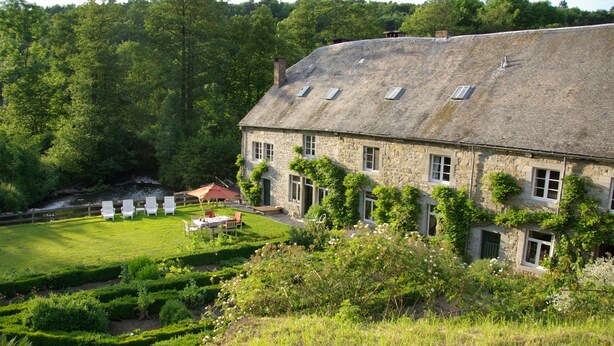 A stone building with a sloped roof, surrounded by a well-maintained garden with hedges and a small pond. - Le Moulin de Resteigne (Tellin)