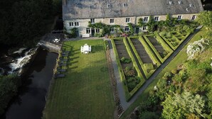 A stone building with multiple windows and a well-maintained garden with geometric hedges and a small pond. - Le Moulin de Resteigne (Tellin)