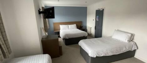 A hotel room with two single beds, a wooden headboard, a desk, and a television on the wall.