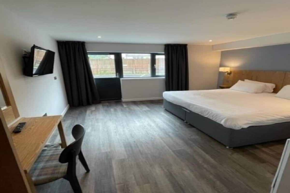 Una habitación de hotel con cama, escritorio, silla, televisión y ventana con cortinas.