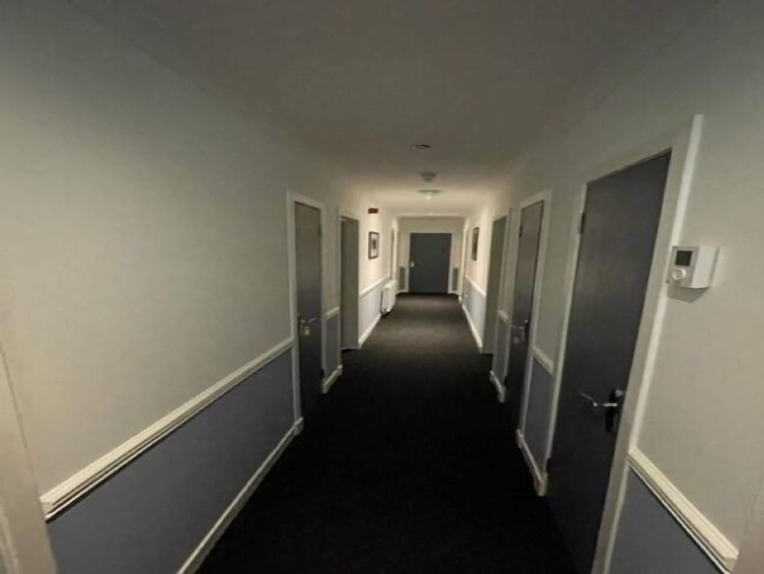 A narrow, dimly lit hallway with doors on both sides, leading to a dark room at the end.