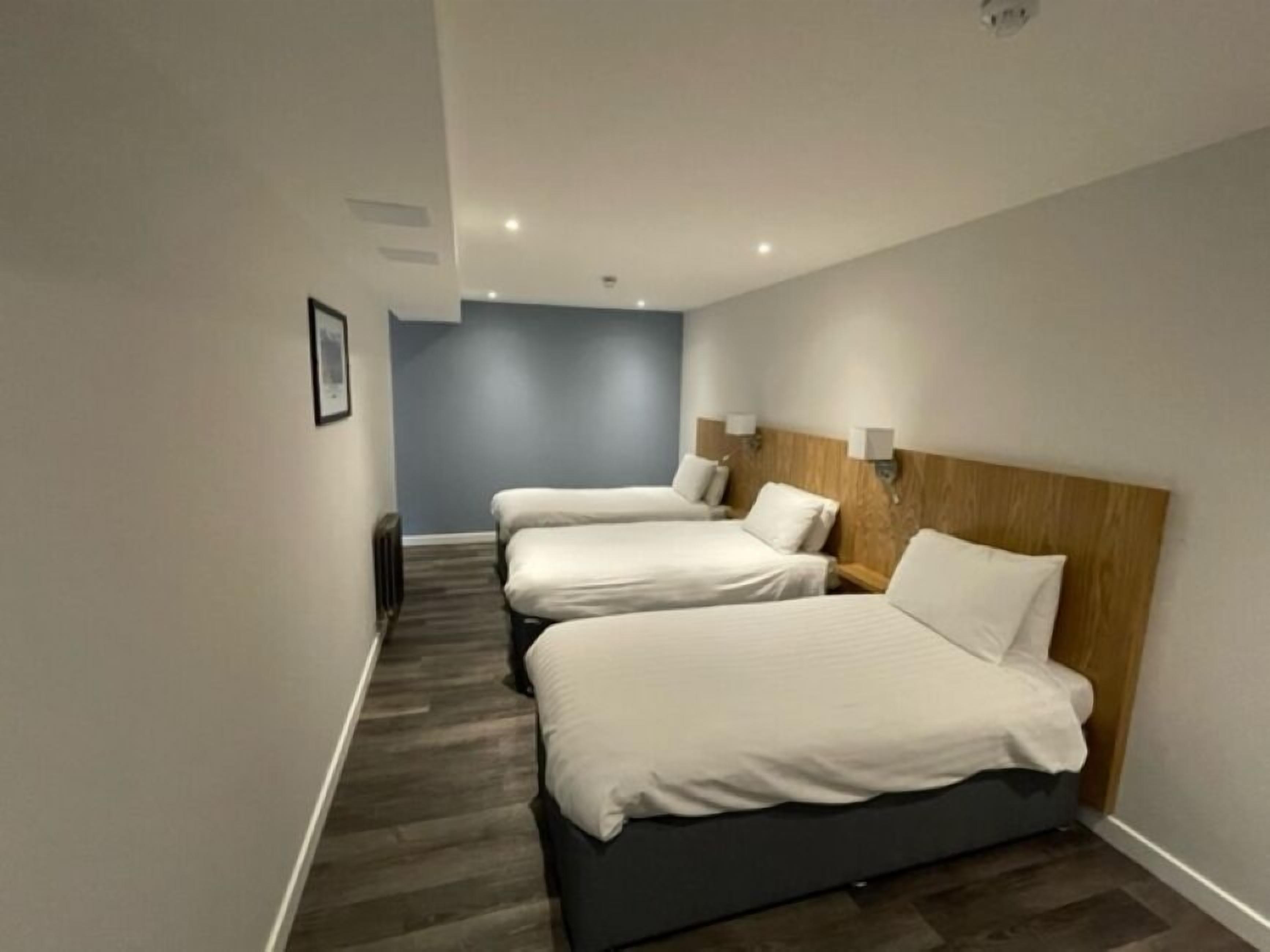 A hotel room with three single beds, a wooden headboard, and a dark floor.