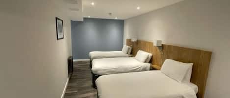 A hotel room with three single beds, a wooden headboard, and a dark floor.