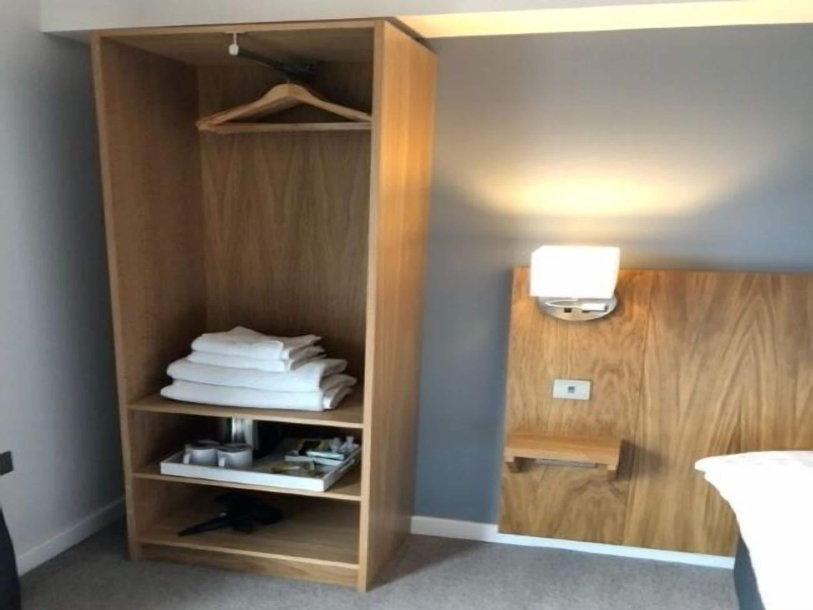 A wooden wardrobe with a hanging space, a shelf with folded towels, and a wall-mounted light fixture.