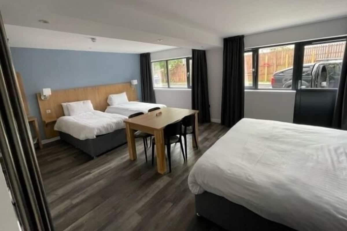 Habitación de hotel con dos camas individuales, un escritorio de madera y un ventanal con vistas al exterior.