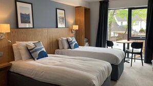 Een hotelkamer met twee bedden, een tafeltje, een stoel en een raam met gordijnen.