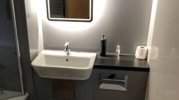 Ein modernes Badezimmer mit einem weißen Waschbecken, einem Spiegel mit Beleuchtung, einer Toilette und einem Mülleimer.