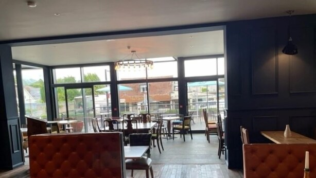 Een restaurant met houten tafels en zitbanken, grote ramen met uitzicht op de stad, en een kroonluchter aan het plafond.