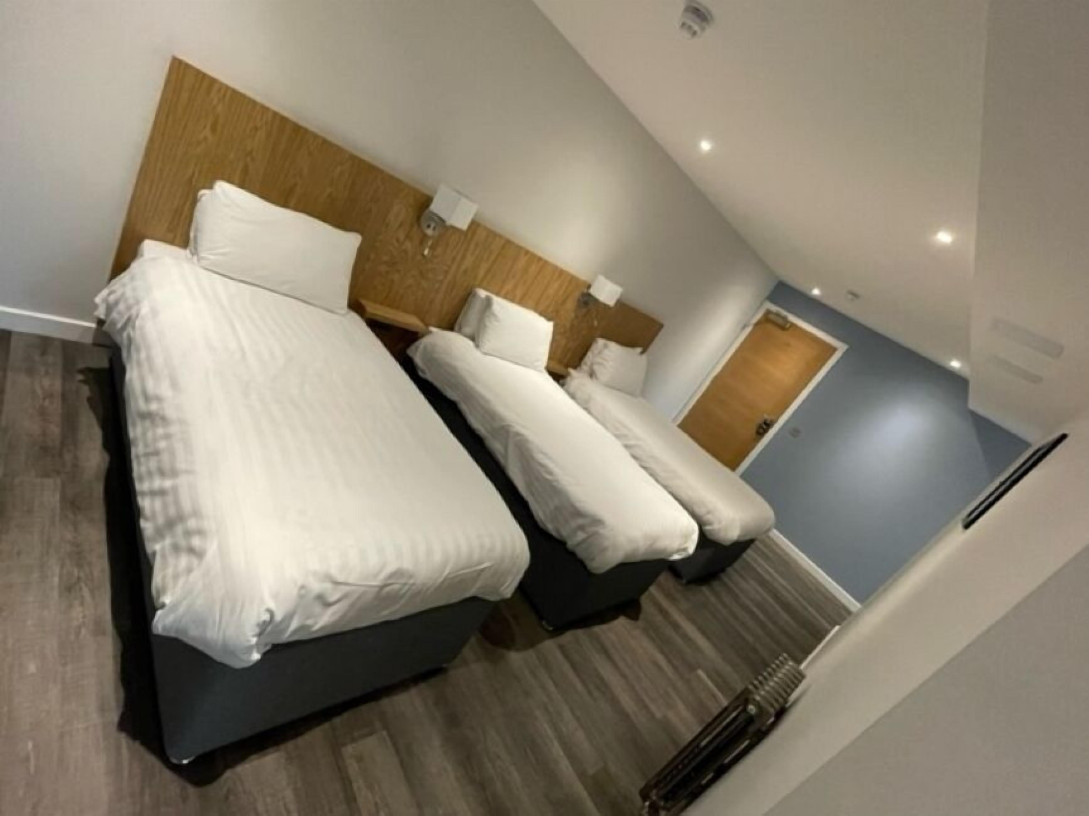 A hotel room with a modern design, featuring a large bed with white linens, a wooden headboard, and a small bedside table.