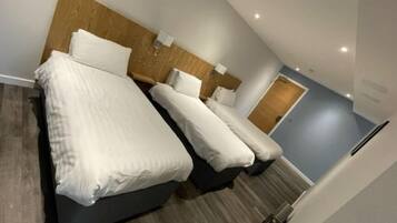 A hotel room with a modern design, featuring a large bed with white linens, a wooden headboard, and a small bedside table.