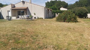 A single-story building with a tiled roof, a satellite dish, and a small garden area with a few potted plants and a bush with red flowers. - Villa Privée Avec Jardin Clos 20 Minutes de la Plage (Luchat)