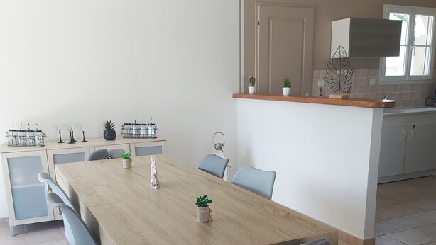 A modern kitchen with a wooden dining table, grey chairs, and a small island with plants. - Villa Privée Avec Jardin Clos 20 Minutes de la Plage (Luchat)