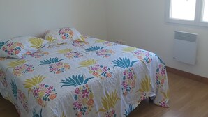 A bed with a floral bedspread in a room with wooden flooring and a window. - Villa Privée Avec Jardin Clos 20 Minutes de la Plage (Luchat)