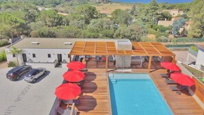 Zona de piscina en la azotea con sombrillas rojas, una piscina y vistas al mar y las colinas.