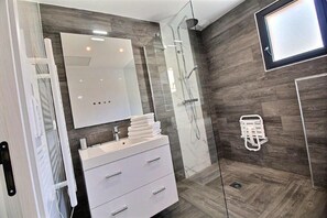 Un baño moderno con cabina de ducha de vidrio, tocador blanco con espejo y perchero.