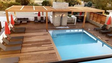 Piscina con muelle de madera, sillas de descanso y una zona de estar cubierta.